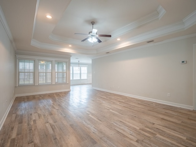 empty room with baseboards, light wood-style flooring, a tray ceiling, and a ceiling fan