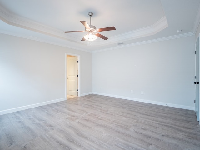 unfurnished room featuring a raised ceiling, crown molding, light wood-style flooring, and baseboards