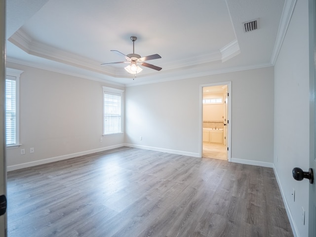 spare room featuring a tray ceiling, visible vents, crown molding, and wood finished floors