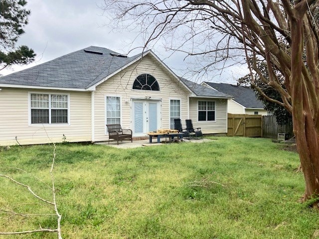 rear view of property featuring a patio, a shingled roof, fence, and a yard