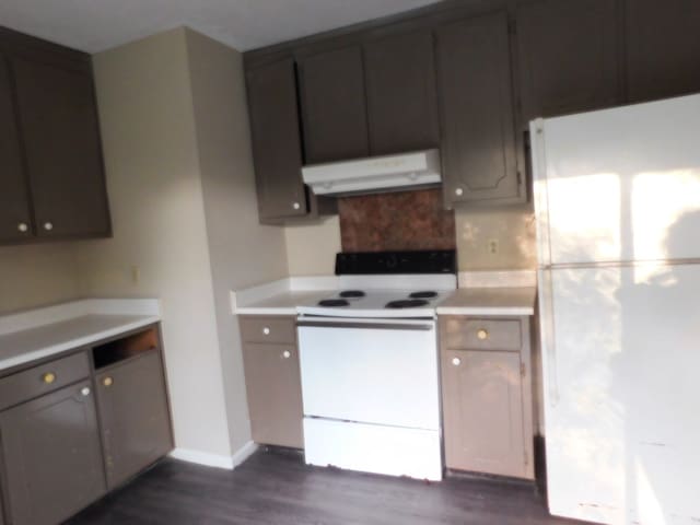 kitchen featuring light countertops, under cabinet range hood, white appliances, and dark wood-style floors