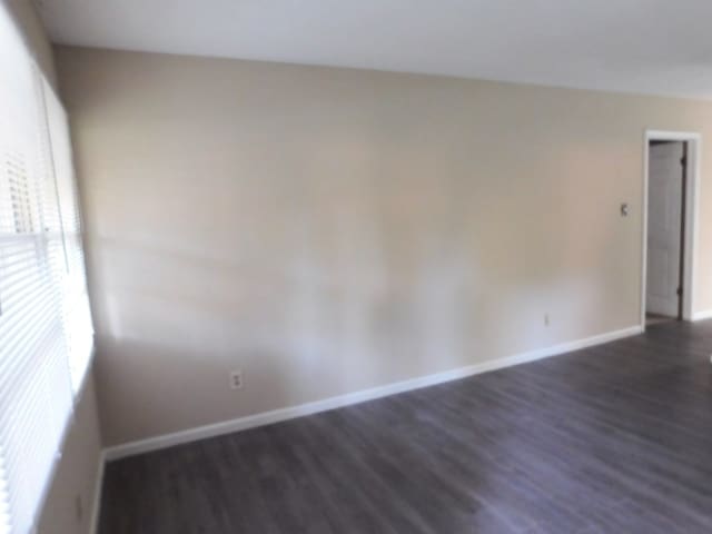 empty room featuring baseboards and dark wood-style floors