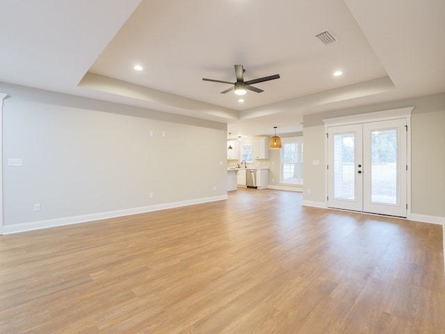 unfurnished living room featuring ceiling fan, light hardwood / wood-style floors, a raised ceiling, and french doors