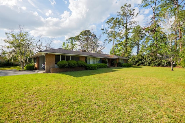 view of front of house featuring brick siding, a front yard, a chimney, a carport, and driveway