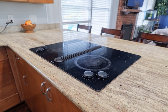 kitchen with black electric cooktop, light stone countertops, brown cabinetry, and a fireplace
