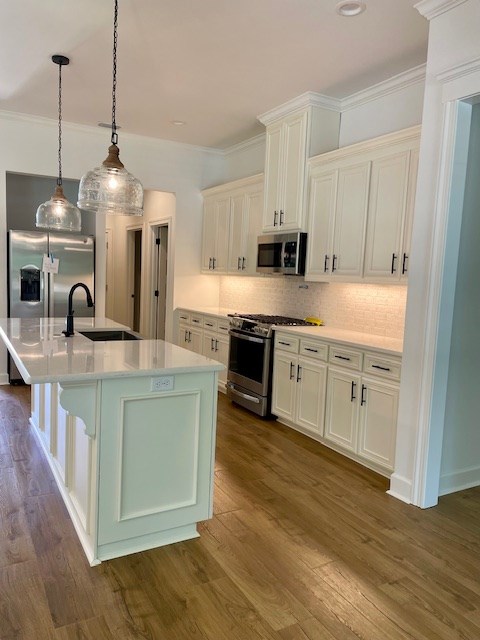 kitchen featuring tasteful backsplash, light countertops, appliances with stainless steel finishes, ornamental molding, and a sink