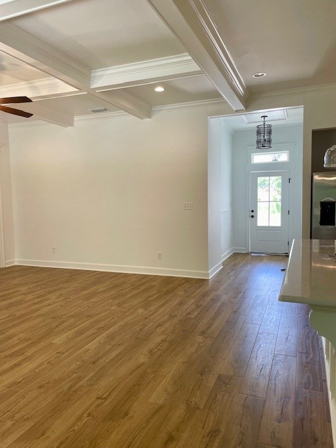 interior space with baseboards, beamed ceiling, wood finished floors, and crown molding