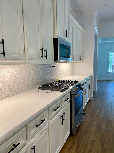 kitchen with dark wood finished floors, light countertops, appliances with stainless steel finishes, ornamental molding, and white cabinetry