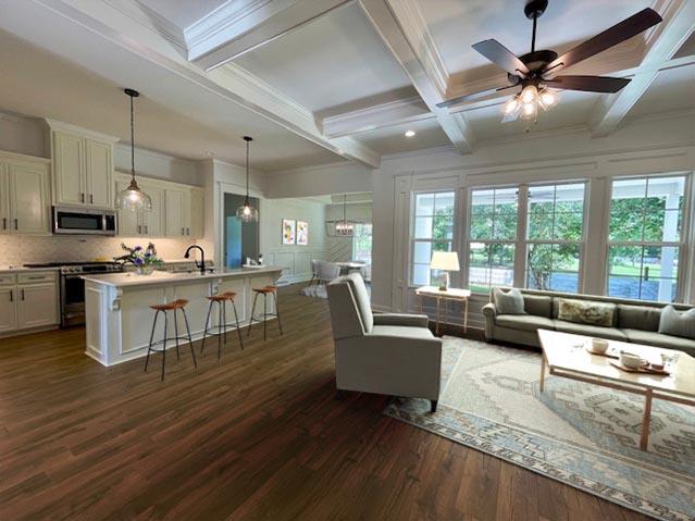 living area with dark wood-style floors, crown molding, ceiling fan, coffered ceiling, and beamed ceiling