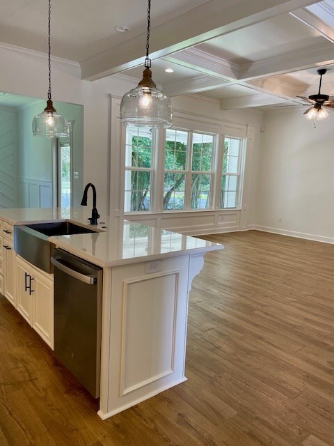 kitchen featuring beam ceiling, a sink, stainless steel dishwasher, and wood finished floors