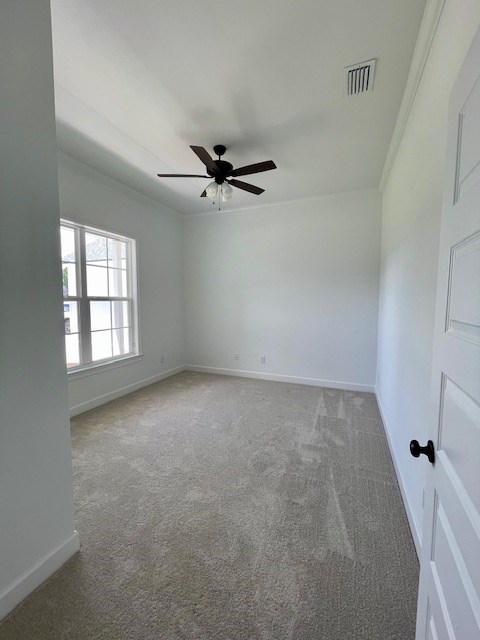 carpeted empty room featuring ornamental molding, visible vents, ceiling fan, and baseboards