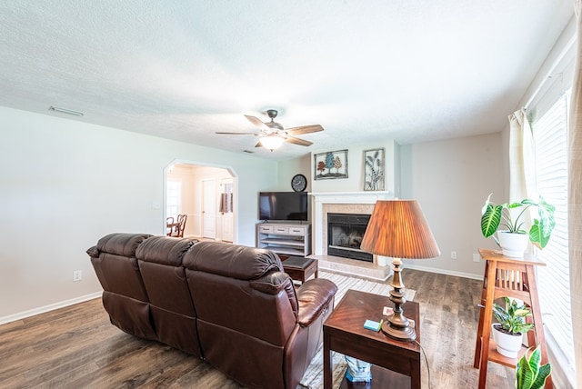 living room with wood finished floors, baseboards, ceiling fan, a fireplace with raised hearth, and arched walkways