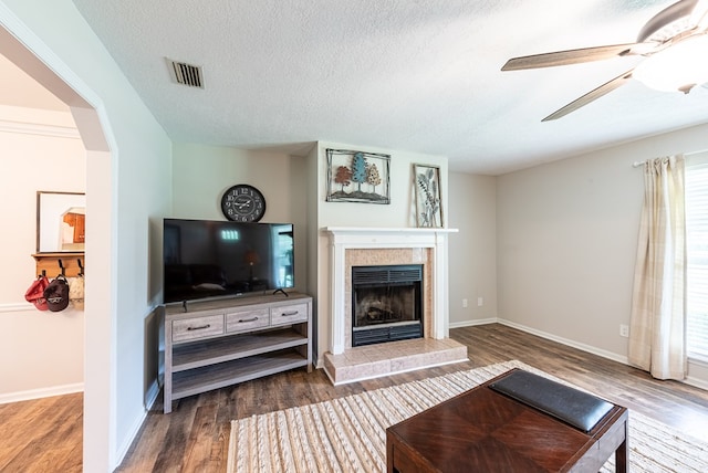 living area with visible vents, wood finished floors, a textured ceiling, a tile fireplace, and a ceiling fan