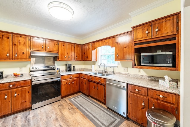kitchen featuring brown cabinetry, ornamental molding, light wood-type flooring, a sink, and appliances with stainless steel finishes