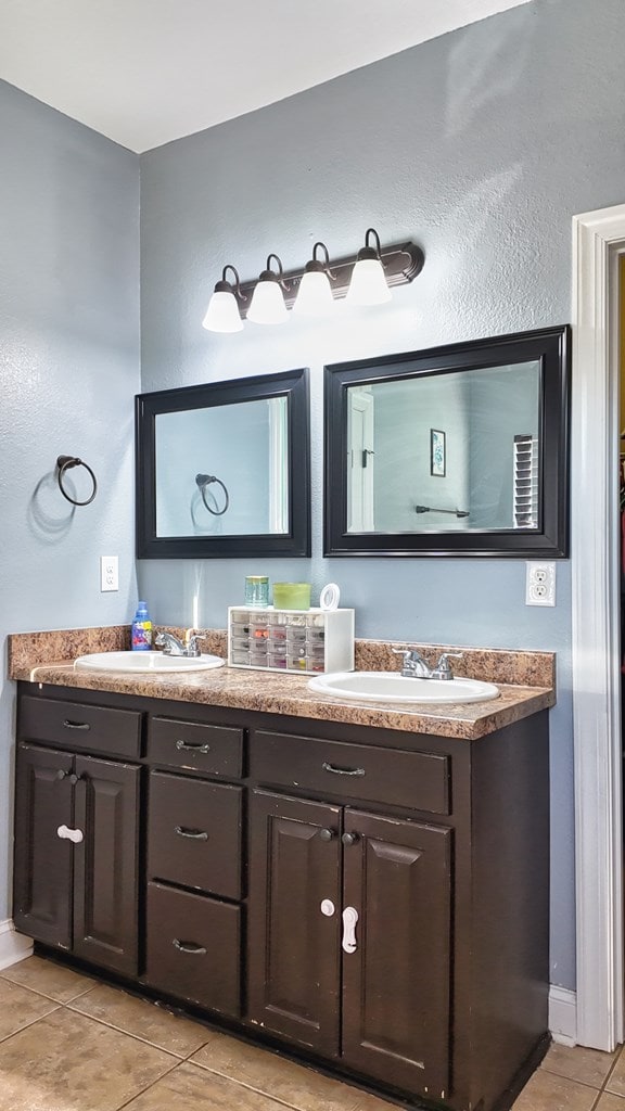 full bath with a sink, baseboards, double vanity, and tile patterned floors