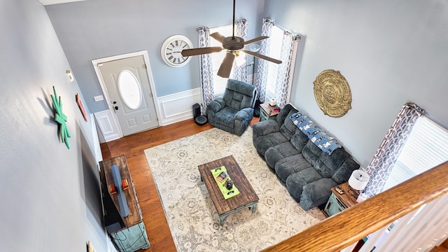 living area featuring ceiling fan, wood finished floors, wainscoting, and a decorative wall