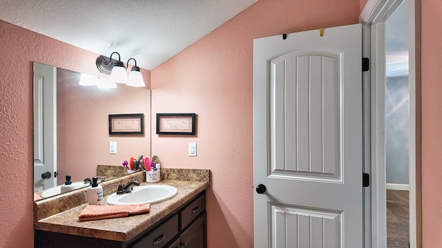 bathroom with vanity, a textured ceiling, vaulted ceiling, and a textured wall