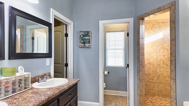 full bathroom with baseboards, toilet, a tile shower, tile patterned floors, and vanity