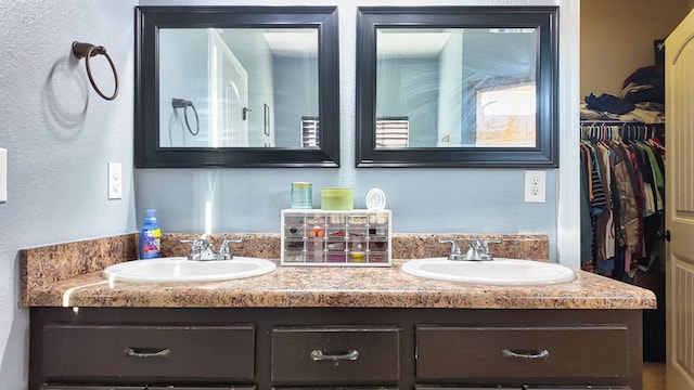 bathroom with a walk in closet, double vanity, and a sink