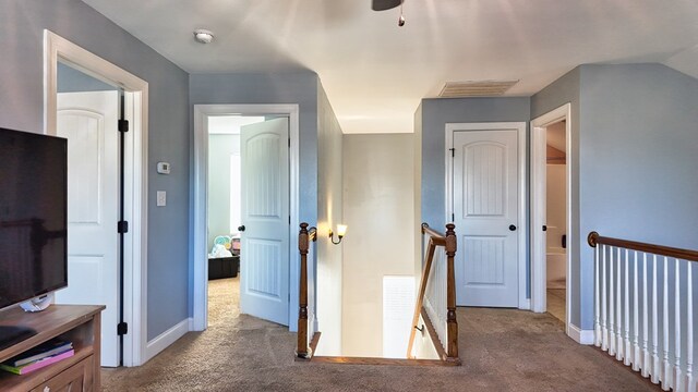 hall featuring an upstairs landing, visible vents, carpet floors, and baseboards