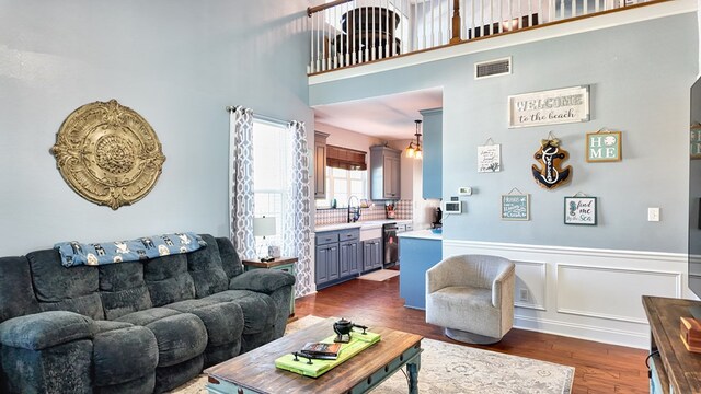 living room featuring visible vents, a high ceiling, dark wood-style flooring, wainscoting, and a decorative wall