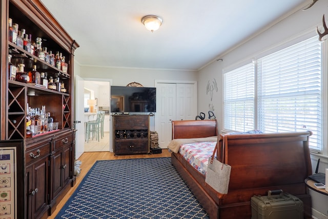 bedroom with light wood-style flooring, a bar, and ornamental molding