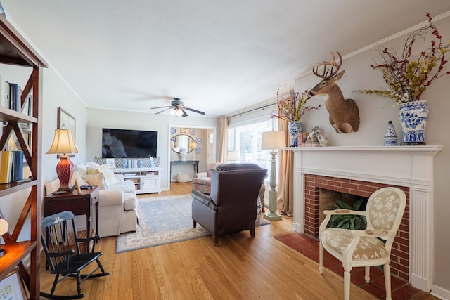 living area with a fireplace, ceiling fan, wood finished floors, and ornamental molding