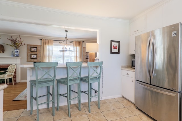 kitchen with ornamental molding, freestanding refrigerator, a breakfast bar area, white cabinets, and light countertops