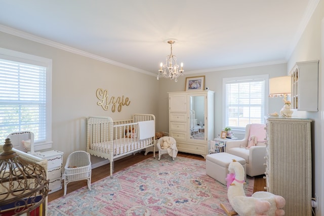 bedroom with ornamental molding, a crib, an inviting chandelier, and wood finished floors