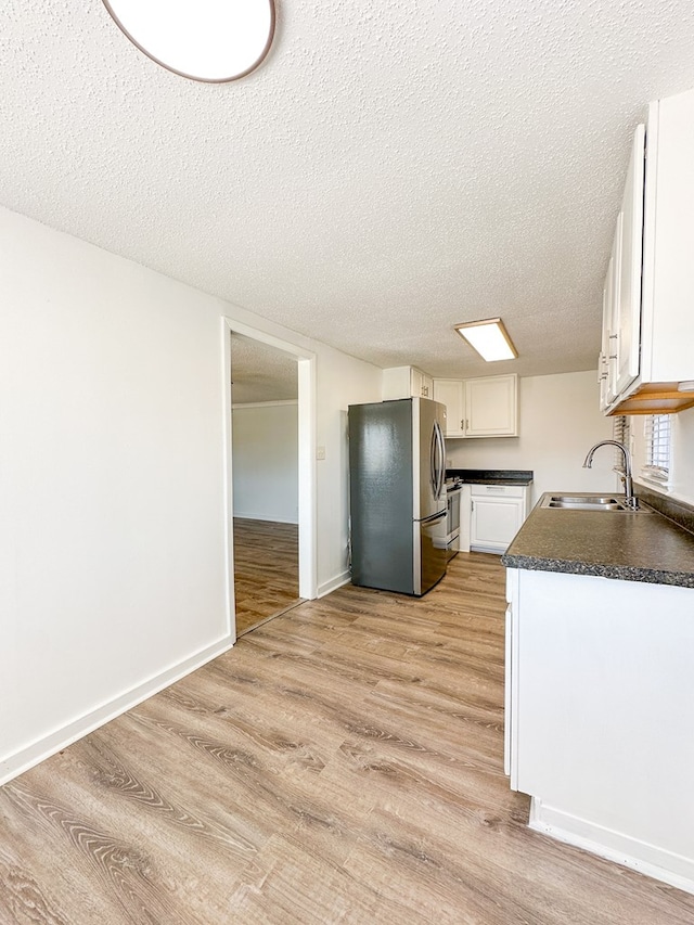 kitchen featuring sink, stainless steel fridge, light hardwood / wood-style floors, a textured ceiling, and white cabinets