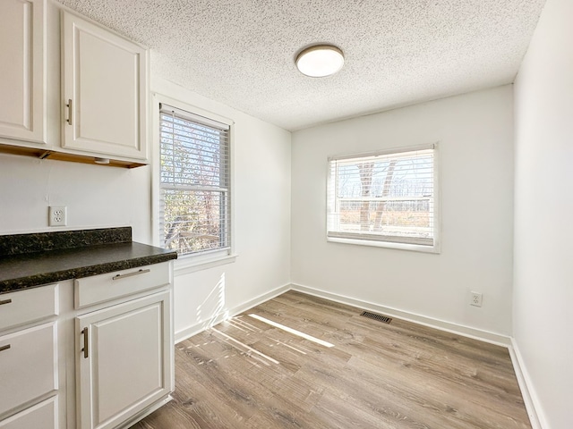 interior space featuring light wood-type flooring, a textured ceiling, and white cabinets