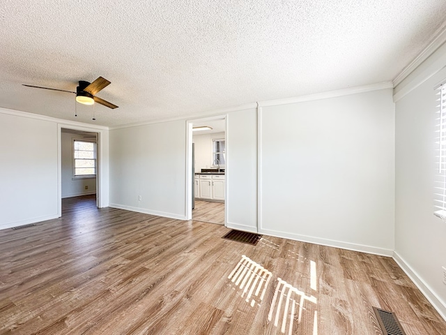 empty room with ornamental molding, ceiling fan, a textured ceiling, and light hardwood / wood-style floors