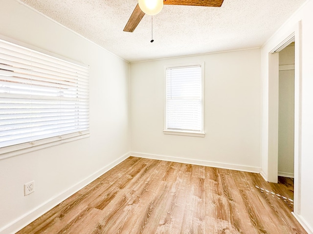 empty room featuring ceiling fan, a healthy amount of sunlight, a textured ceiling, and light hardwood / wood-style flooring