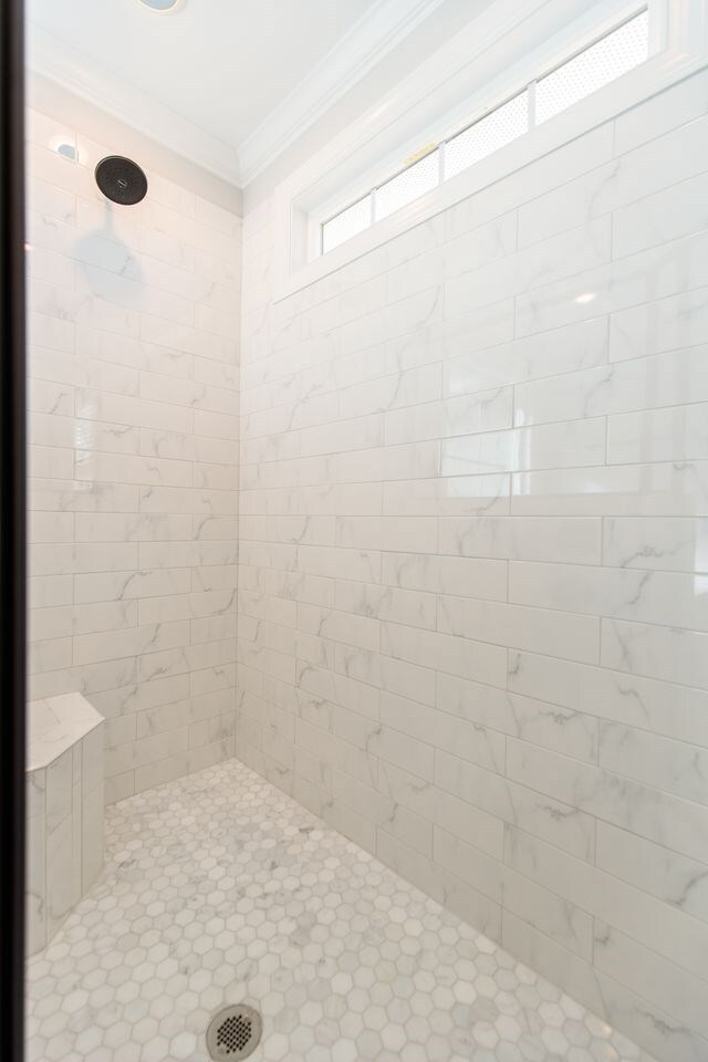 bathroom with a tile shower and crown molding