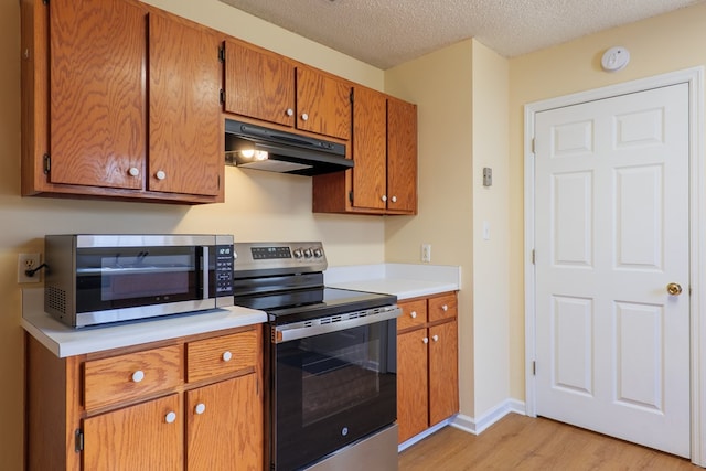 kitchen with a textured ceiling, stainless steel appliances, and light hardwood / wood-style floors