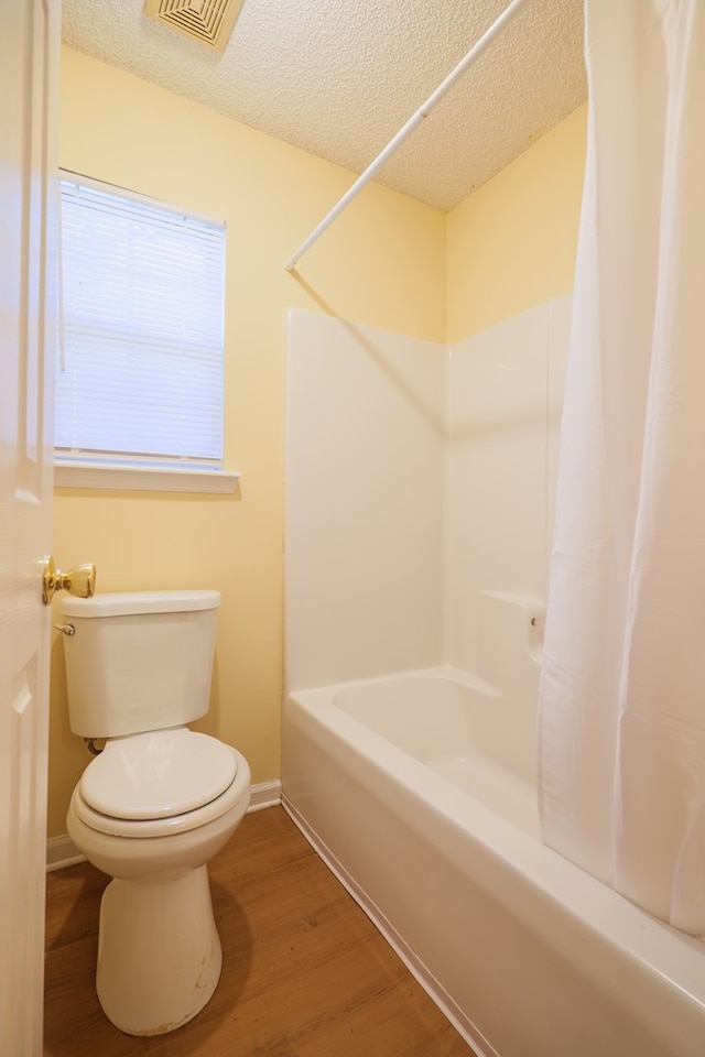 bathroom with hardwood / wood-style floors, toilet, a textured ceiling, and shower / tub combo with curtain