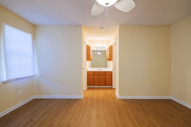 empty room with a textured ceiling, light hardwood / wood-style flooring, ceiling fan, and sink