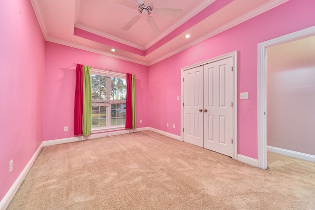 unfurnished bedroom with ceiling fan, light colored carpet, ornamental molding, and a tray ceiling