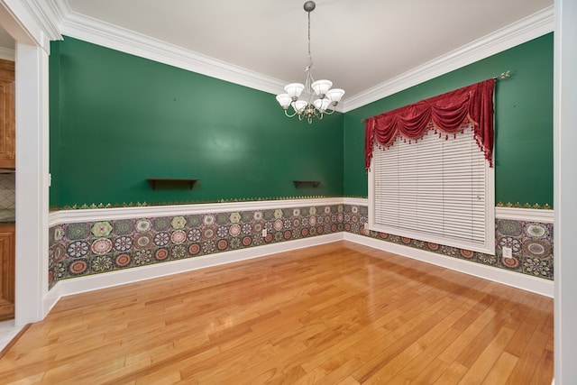 empty room with hardwood / wood-style floors, ornamental molding, and an inviting chandelier