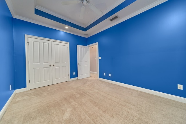 unfurnished bedroom with crown molding, ceiling fan, a tray ceiling, light colored carpet, and a closet