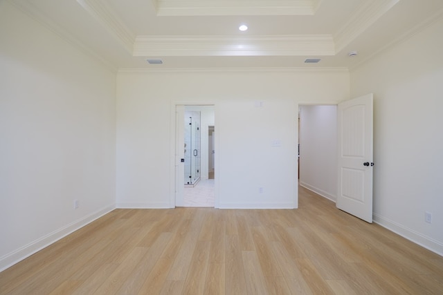empty room featuring a raised ceiling, crown molding, light wood finished floors, and baseboards