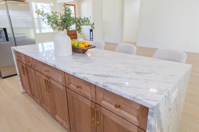 kitchen featuring stainless steel fridge with ice dispenser, a center island, brown cabinetry, and light stone counters
