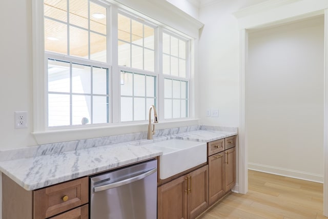 kitchen with stainless steel dishwasher, light stone countertops, a sink, brown cabinets, and light wood finished floors