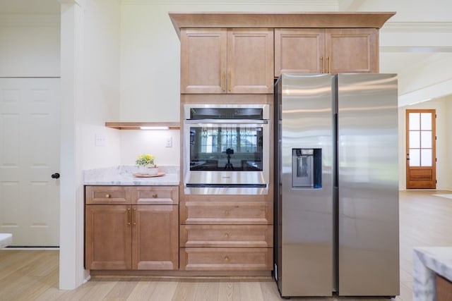 kitchen featuring light wood-type flooring, ornamental molding, light stone countertops, brown cabinetry, and stainless steel appliances