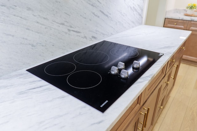 room details featuring brown cabinets, black electric stovetop, and light stone counters