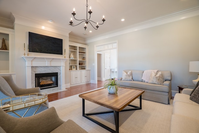 living room featuring a premium fireplace, an inviting chandelier, built in features, ornamental molding, and light hardwood / wood-style flooring