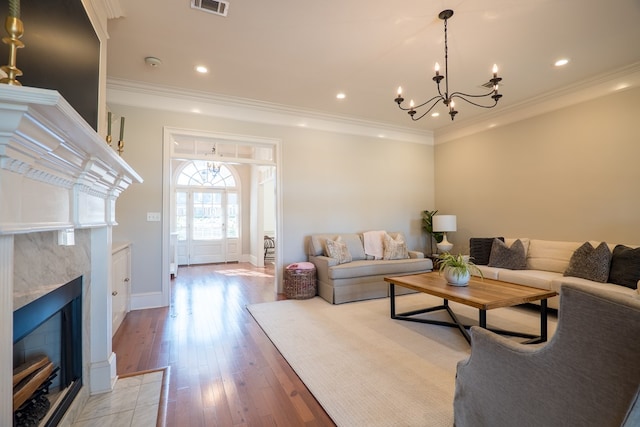 living room featuring light wood-type flooring, a fireplace, an inviting chandelier, and ornamental molding