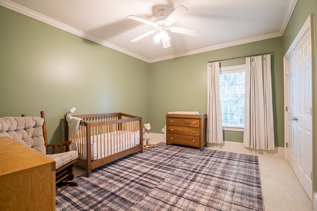 carpeted bedroom featuring ceiling fan, ornamental molding, a closet, and a crib