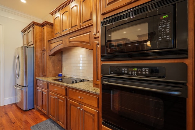 kitchen featuring tasteful backsplash, ornamental molding, light hardwood / wood-style flooring, light stone counters, and black appliances