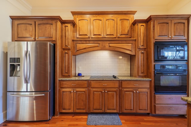 kitchen with light stone countertops, decorative backsplash, hardwood / wood-style flooring, and black appliances